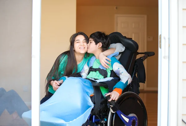 Sister kissing and hugging disabled little brother in wheelchair