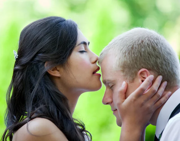 Biracial bride kissing Caucasian groom on forehead