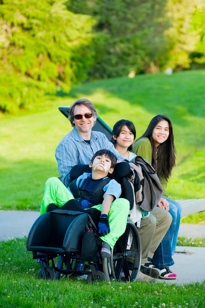 Disabled boy in wheelchair with family outdoors on sunny day sit