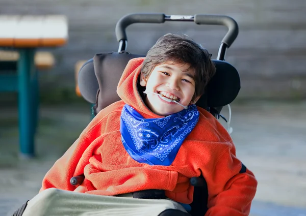 Handsome, happy biracial eight year old boy smiling in wheelchai