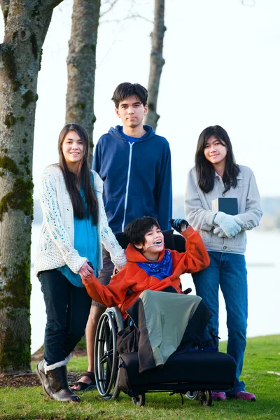 Disabled little boy in wheelchair surrounded by brother and sist