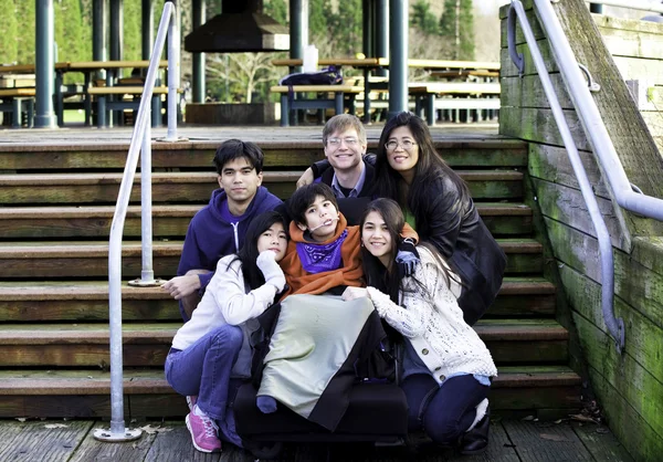 Interracial family surrounding disabled boy in wheelchair outdoo