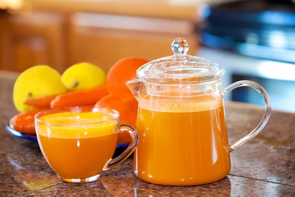 One cup of orange colored juice on kitchen counter with fruit an
