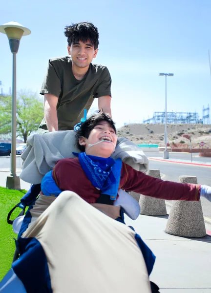 Big brother pushing happy disabled boy in wheelchair