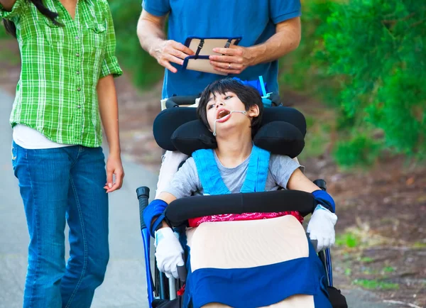 Disabled child in wheelchair outdoors with caregivers or family