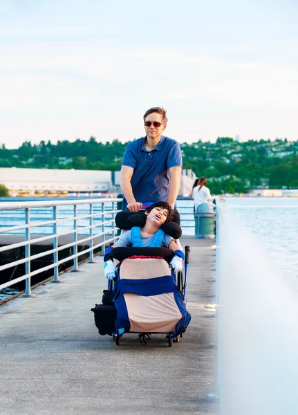 Disabled child in wheelchair outdoors by lake with family