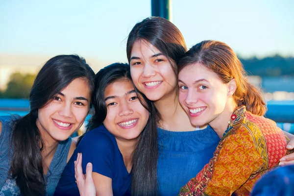 Group of four young women smiling together by lake