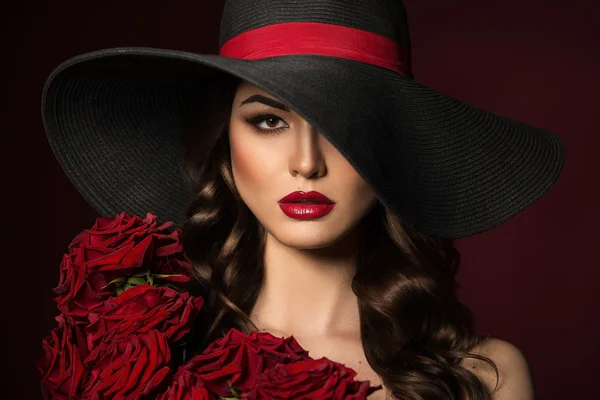 Portrait of a beautiful woman in a black hat with red roses on t