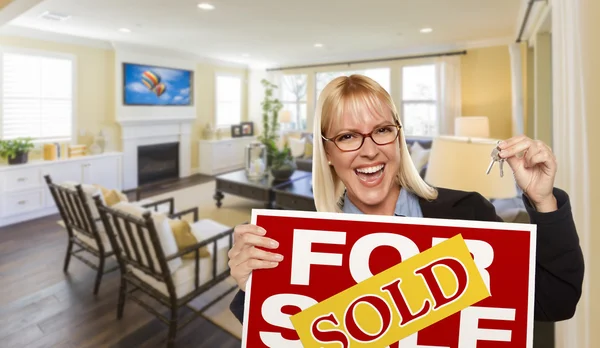 Young Woman Holding Sold Sign and Keys Inside Living Room