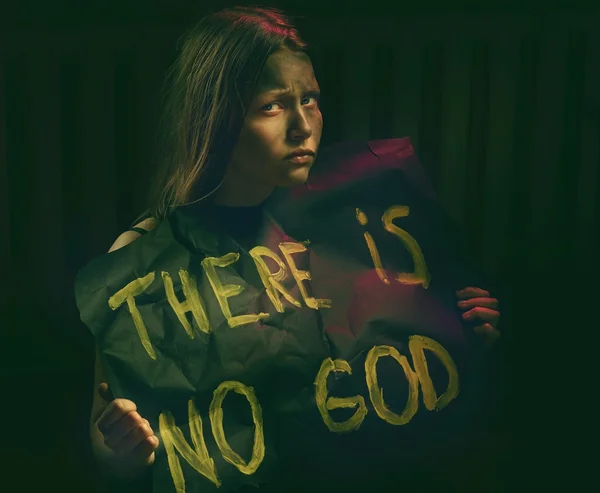 Teen girl with dirty face holding banner with a text - There is no God. Atheistic concept.