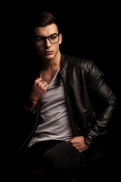 Man in black leather jacket wearing glasses pulling his shirt