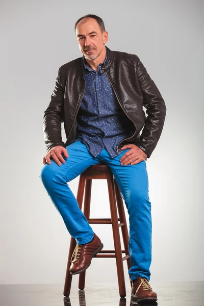 Full body picture of seated old man in leather jacket