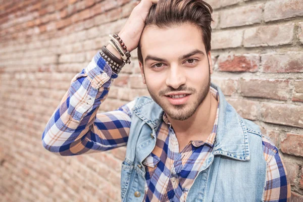 Young man fixing his hair, leaning on a brick wall