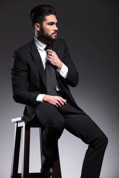 Business man sitting on a stool fixing his tie