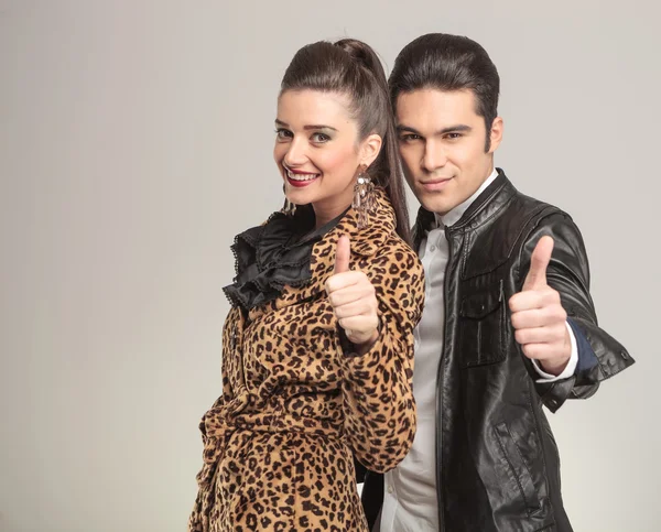 Fashion couple smiling and showing the thumbs up gesture.