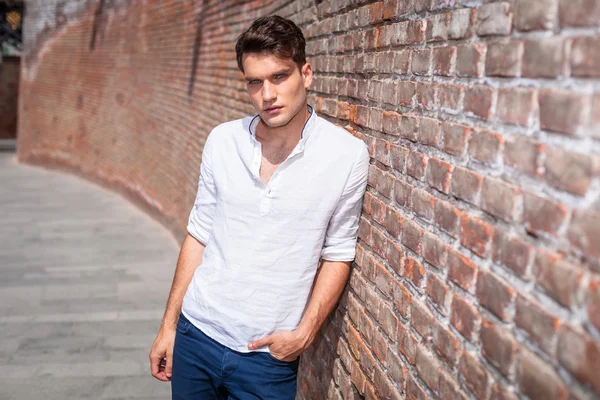 Attractive young fashion man leaning on a brick wall