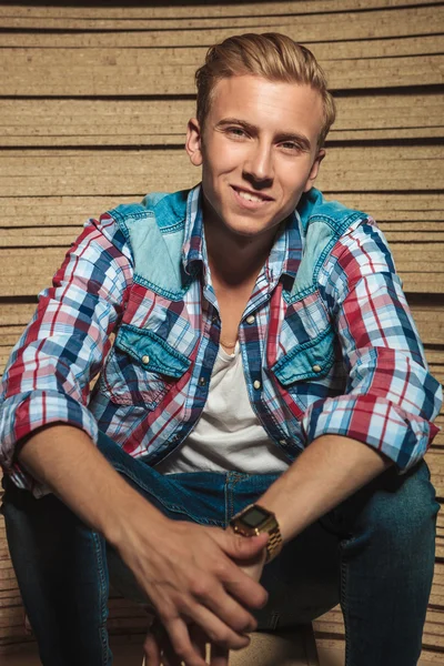 Blonde young man sitting in studio while smiling