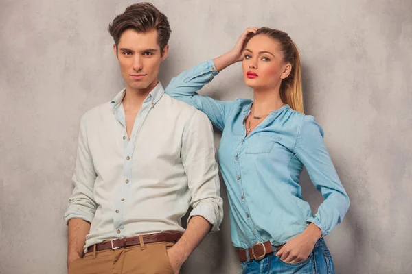Couple posing in studio with hands in pockets while leaning and
