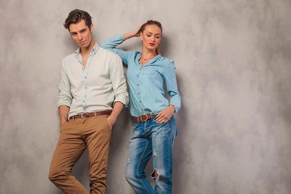 Man pose in studio with hands in pockets while woman is resting