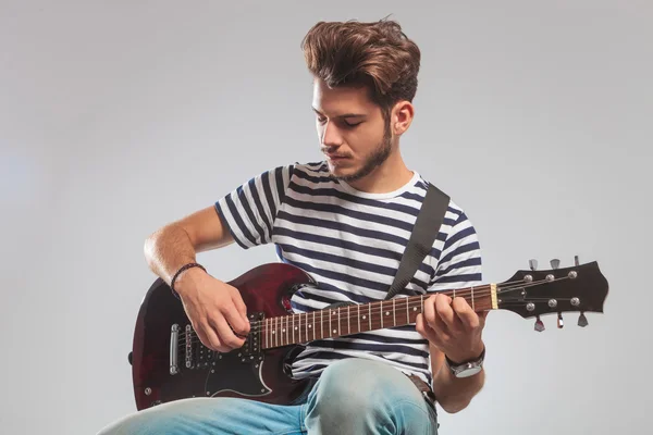 Guitarist pose seated in studio while playing guitar