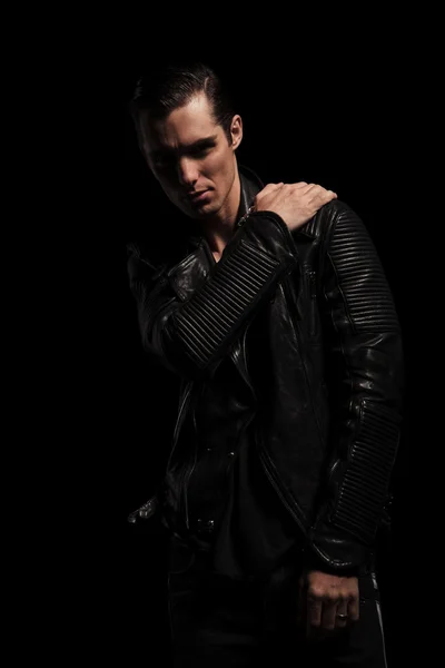 Confident rocker in black leather jacket posing in dark studio
