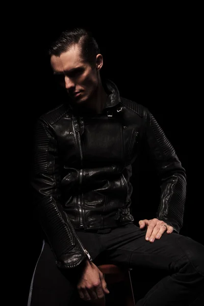 Punk model in leather jacket posing seated in dark studio
