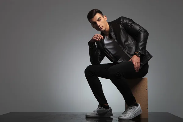 Male model in leather jacket posing seated while thinking