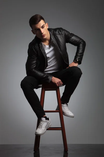 Model in leather jacket posing seated in studio while resting