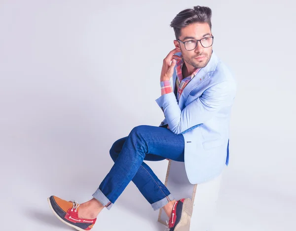 Hipster posing seated with legs crossed while touching his neck