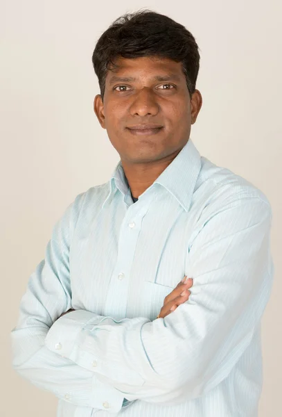 An Indian or South Asian business executive with folded arms looking to camera. On grey background.