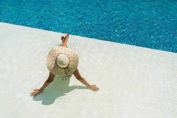 Beautiful woman in a hat sitting on the edge of the pool