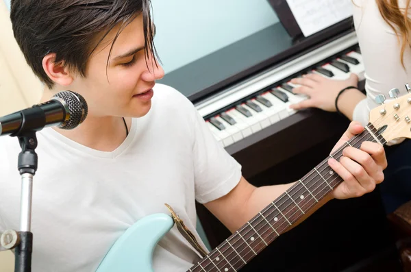 Teenage boy playing electric guitar and singing girl piano