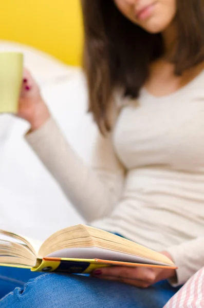 Beautiful girl sitting at home, reading book and drinking coffee