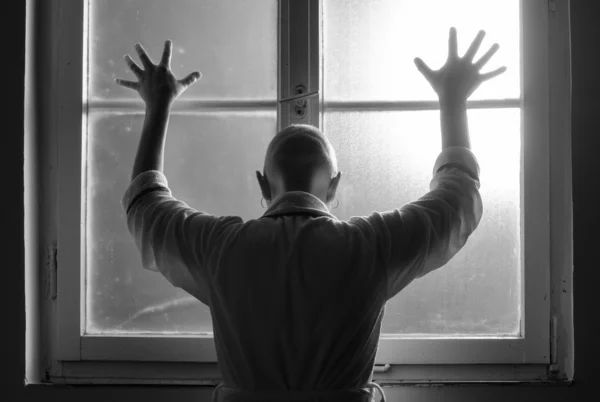 Bald woman suffering from cancer leaning on the hospital window