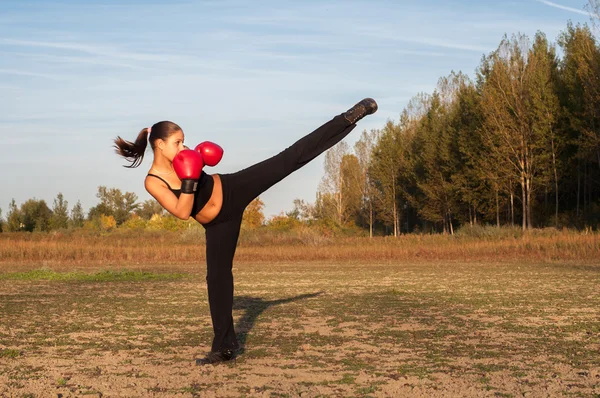 Beautiful kickboxing girl exercising high kick in the nature on sunny summer day