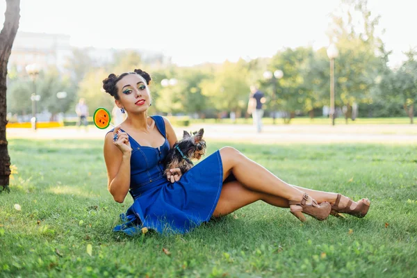 Bright makeup beautiful girl with Yorkshire Terrier seating on the grass holding watermelon lollipop.