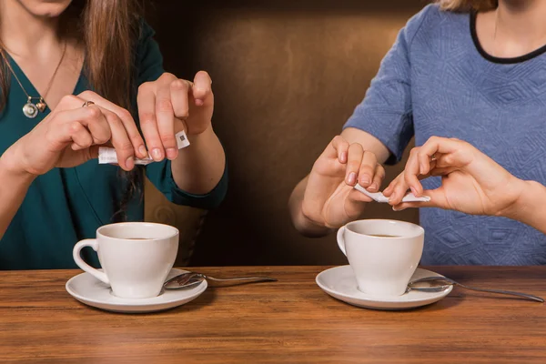 Hands of two women putting sugar in a cup of coffee