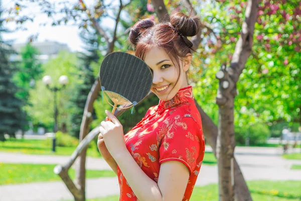 Beautiful asian girl in traditional chinese red dress with bamboo fan.