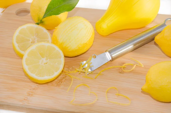 Lemons, squeezer, zest and Zester on wooden cutting board.