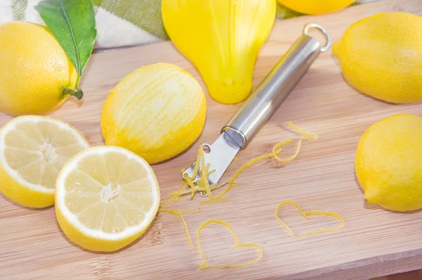 Fresh lemons, squeezer, zest and Zester on wooden cutting board.