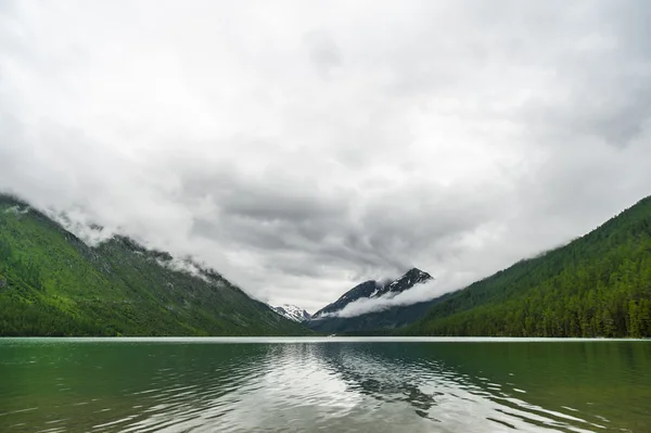 Mountains reflected in the lake with clouds closing peaks. Gorny Altai Russia