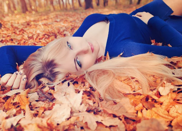 Beautiful young woman lying in a pile of leaves.