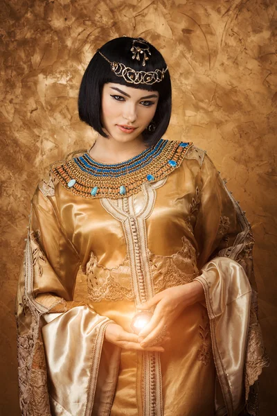 Beautiful Egyptian woman like Cleopatra with magic ball on golden background