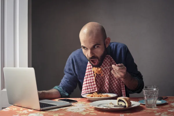 Man eating pasta and checking computer