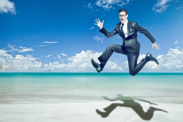 Businessman jumps in black suit on tropical beach.