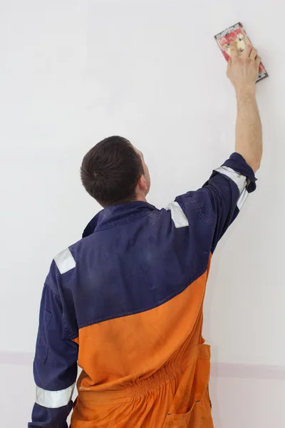Man grinding white wall with sandpaper, back view