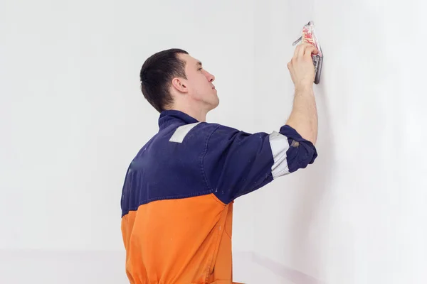 Man grinding white wall with sandpaper