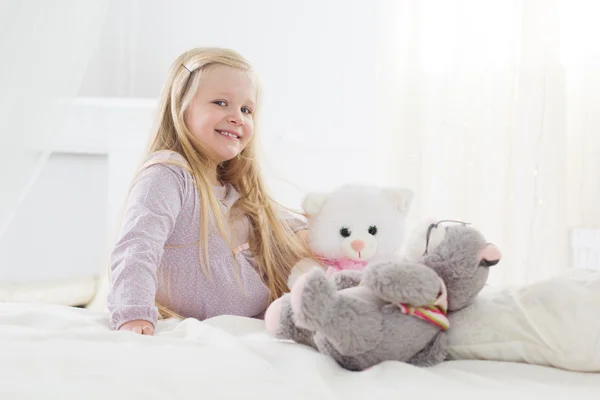 Child girl sitting in the bed with her soft toys