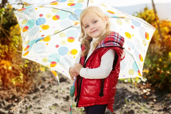 Little girl with umbrella in red vest outdoor