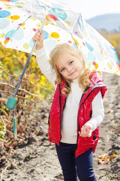 Little girl with umbrella in red vest outdoor